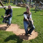 Zwei Teilnehmerinnen schaukeln auf einem Spielplatz auf modifizierten Pferdeschaukeln